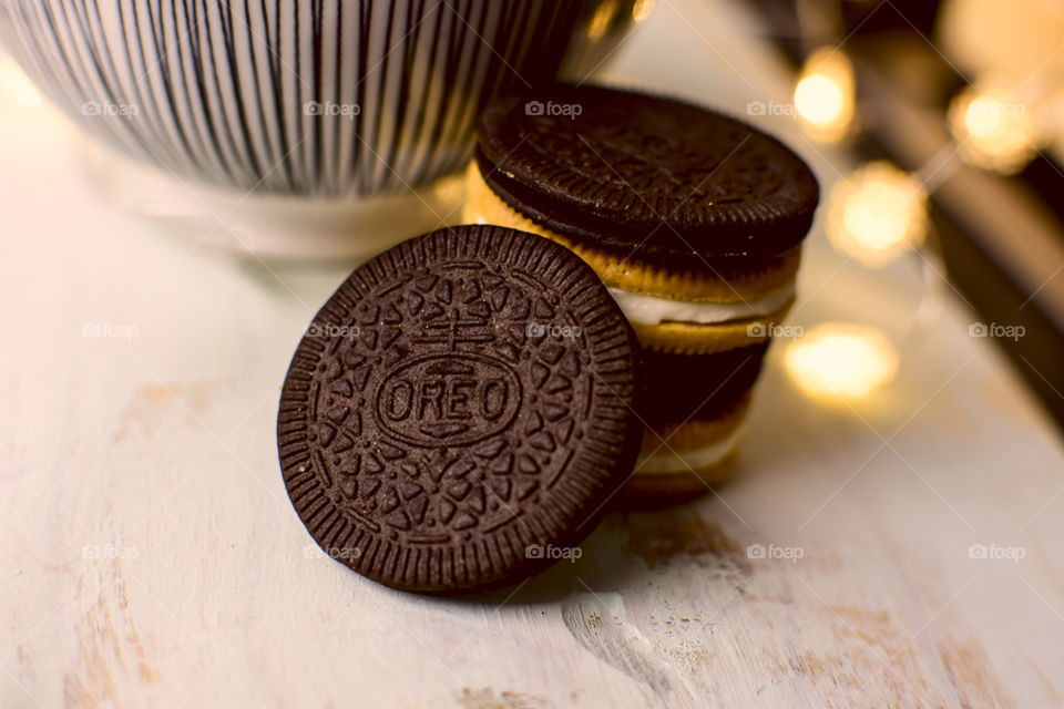 Stack of thin Oreo with cinnamon Oreos on rustic wood with striped bowl and lights in background 