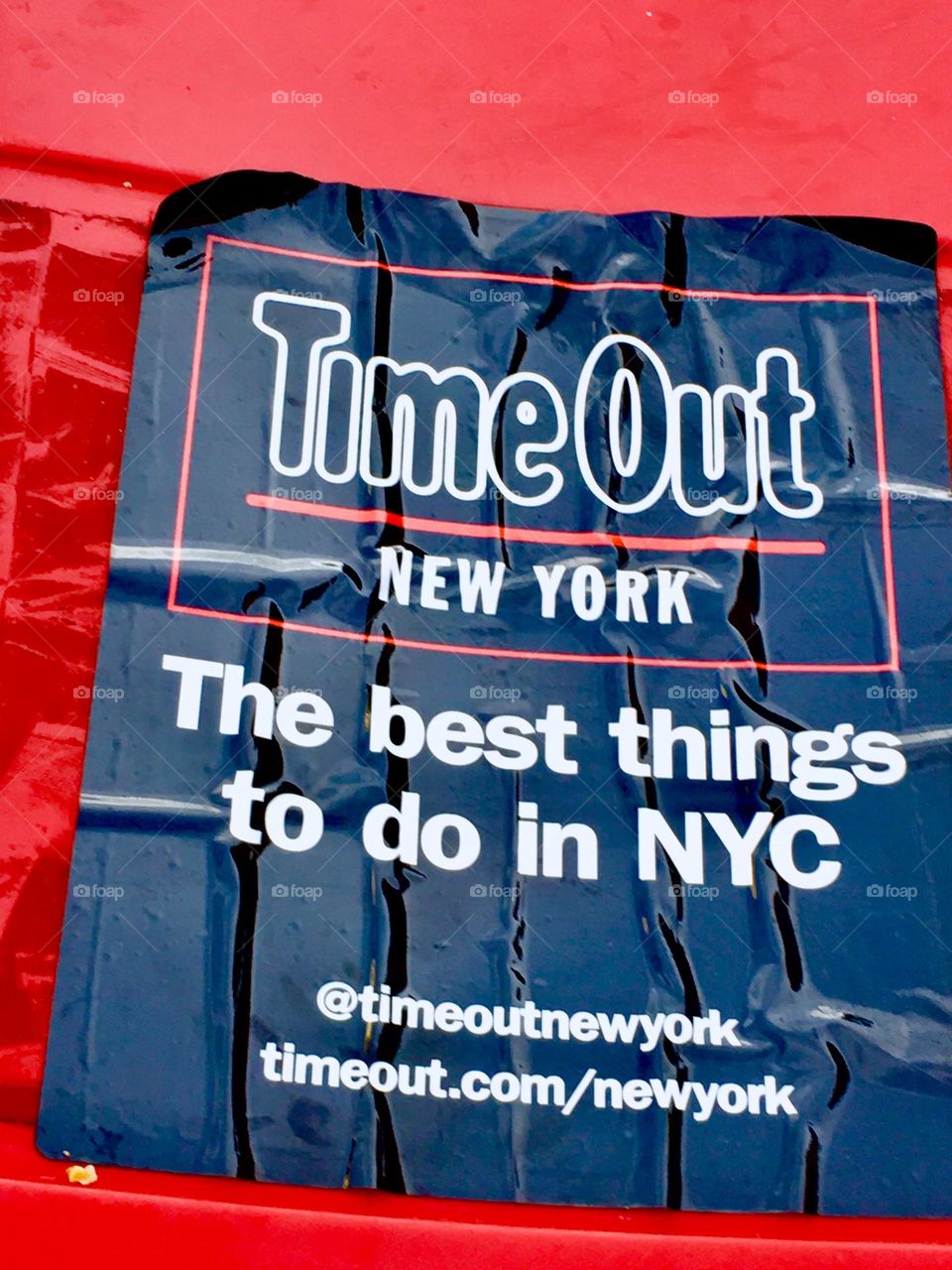 „Time Out New York“ is a popular magazine in NYC that tells when there is whatever interesting thing staged and where. This is a red plastic cover with a label laid out on a sidewalk in LIC, Queens containing the magazine. 2020. Hypnotic Productions