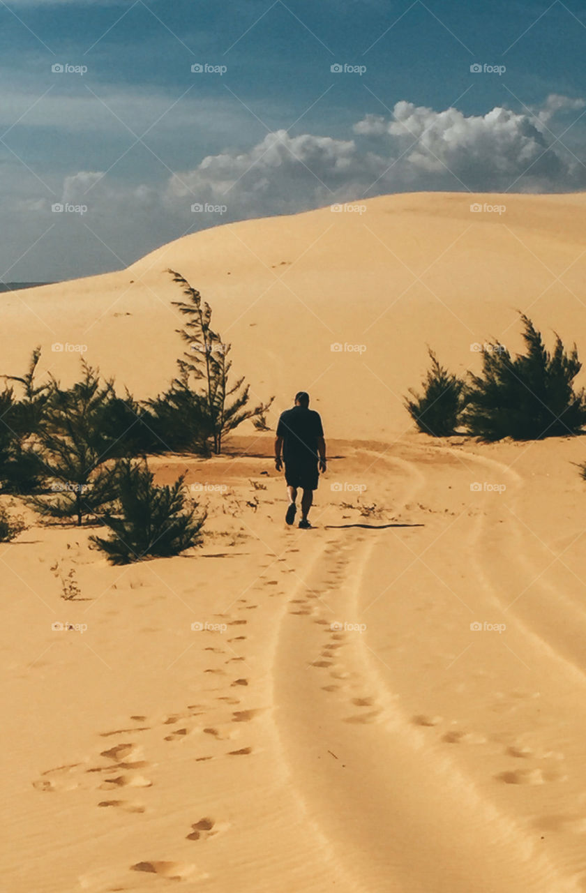 A man is walking on a sand dunes . Footprints printed on the sand . the surrounding bushes . 