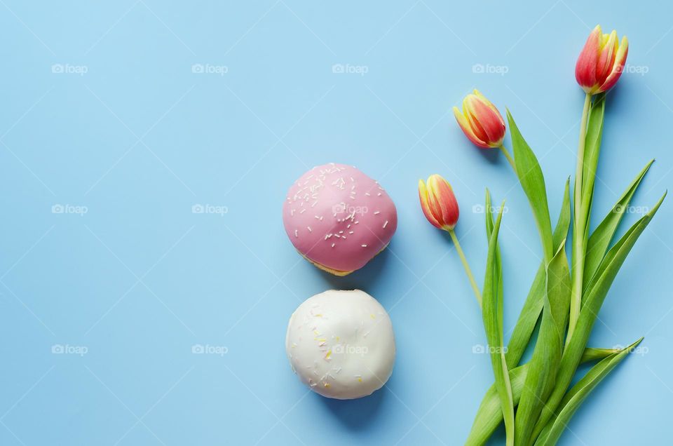 Top view of flowers and sweet donats against blue background close up.