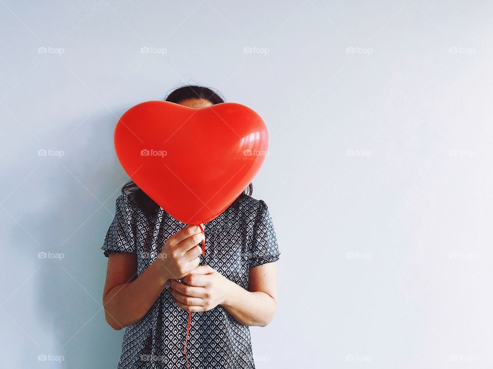 Woman holding heart shaped balloon in front of face. 