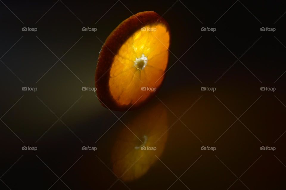 sliced ​​across an orange. the orange is illuminated like a flashlight in the dark and has a reflection from below