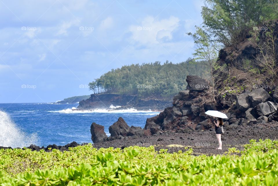 Woman with umbrella, watching the waves while avoiding the sun exposure.