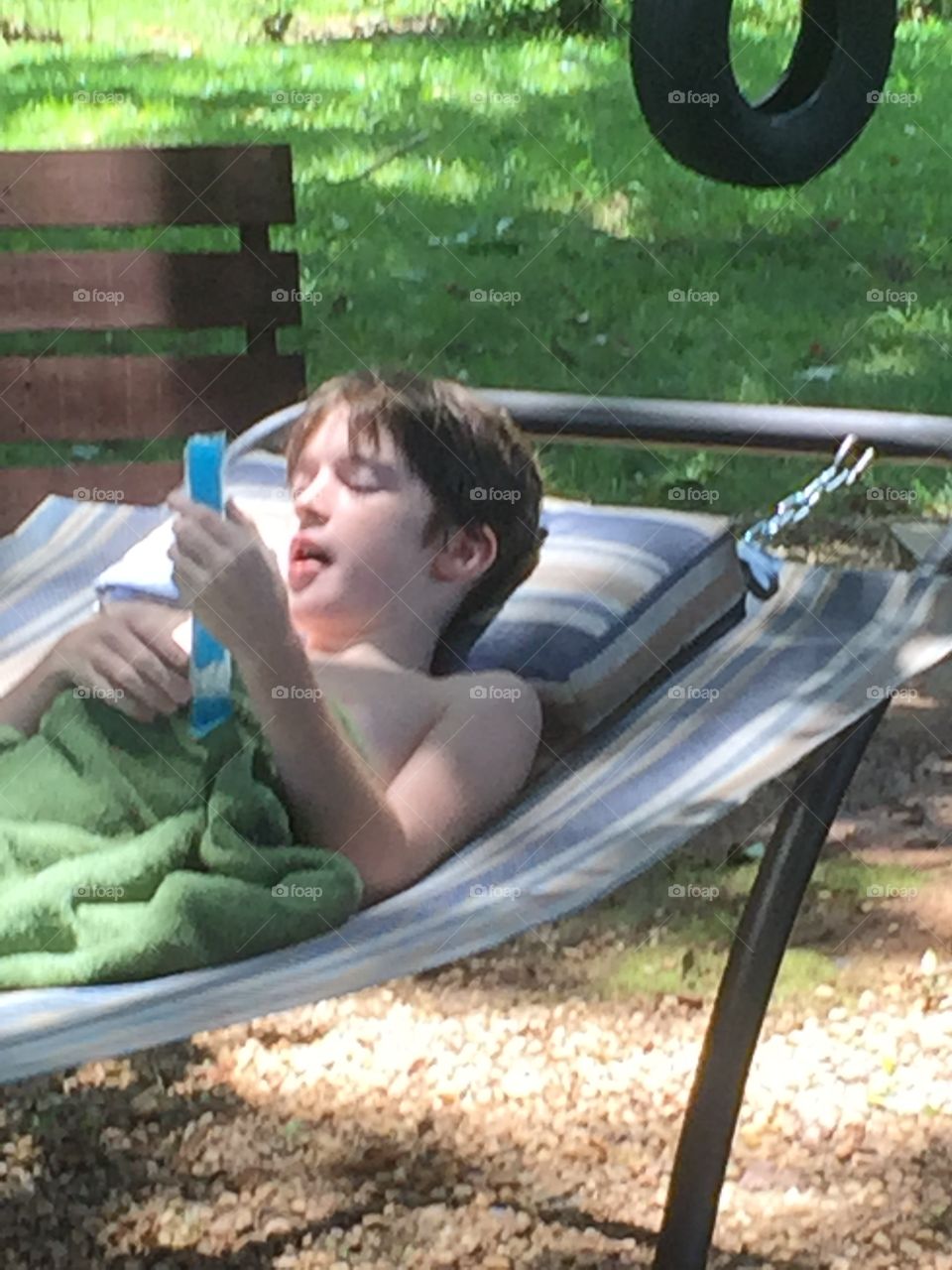 Young boy with a popsicle in the smear lying on a hammock.