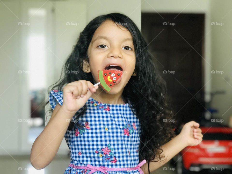 Cute four years girl enjoying by eating watermelon candy lollipop.