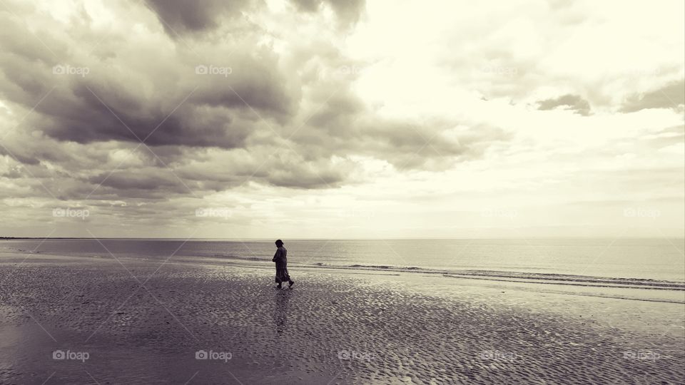 black and white picture of someone walking on the beach under a heavy sky