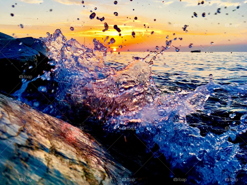 the water breaks on the rocky shore at sunset