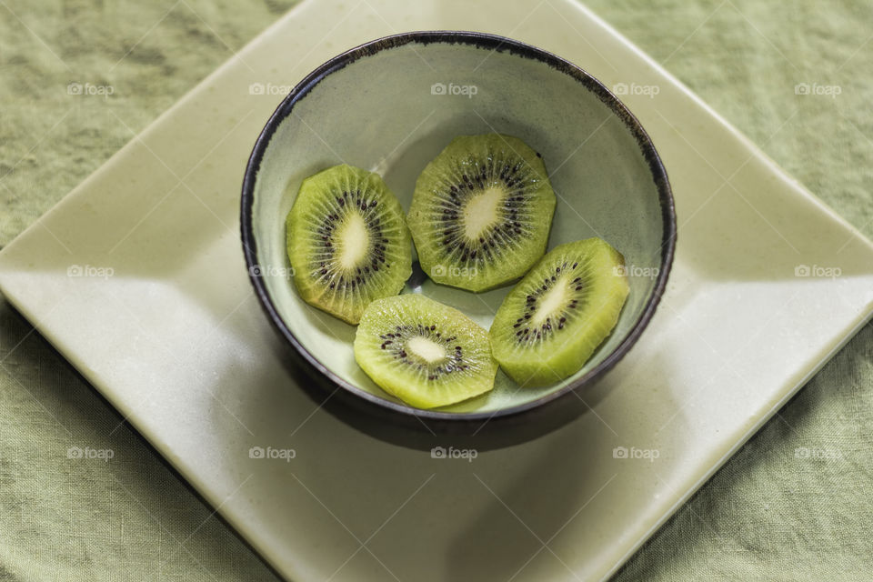 Green kiwis in green bowl on green plate