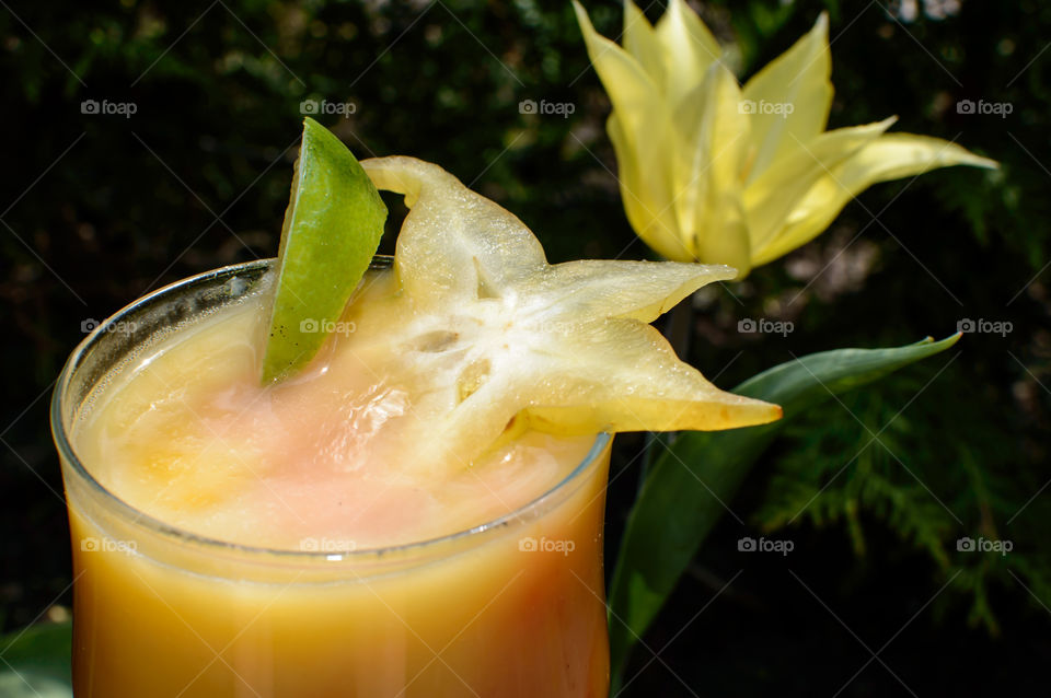 Fresh fruit smoothie with coconut milk, carambola, citrus, mango and berry infusion in garden with lily flowering tulip 