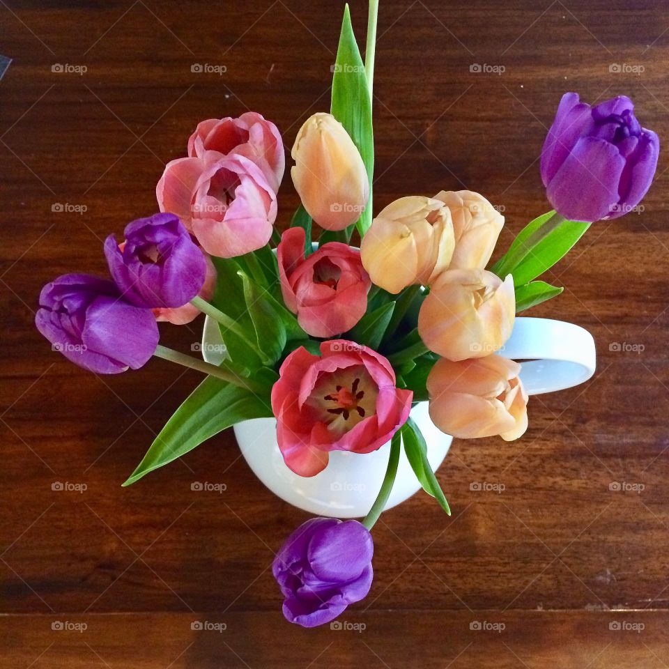 Beautiful colorful spring tulips in white vase on wood kitchen table.