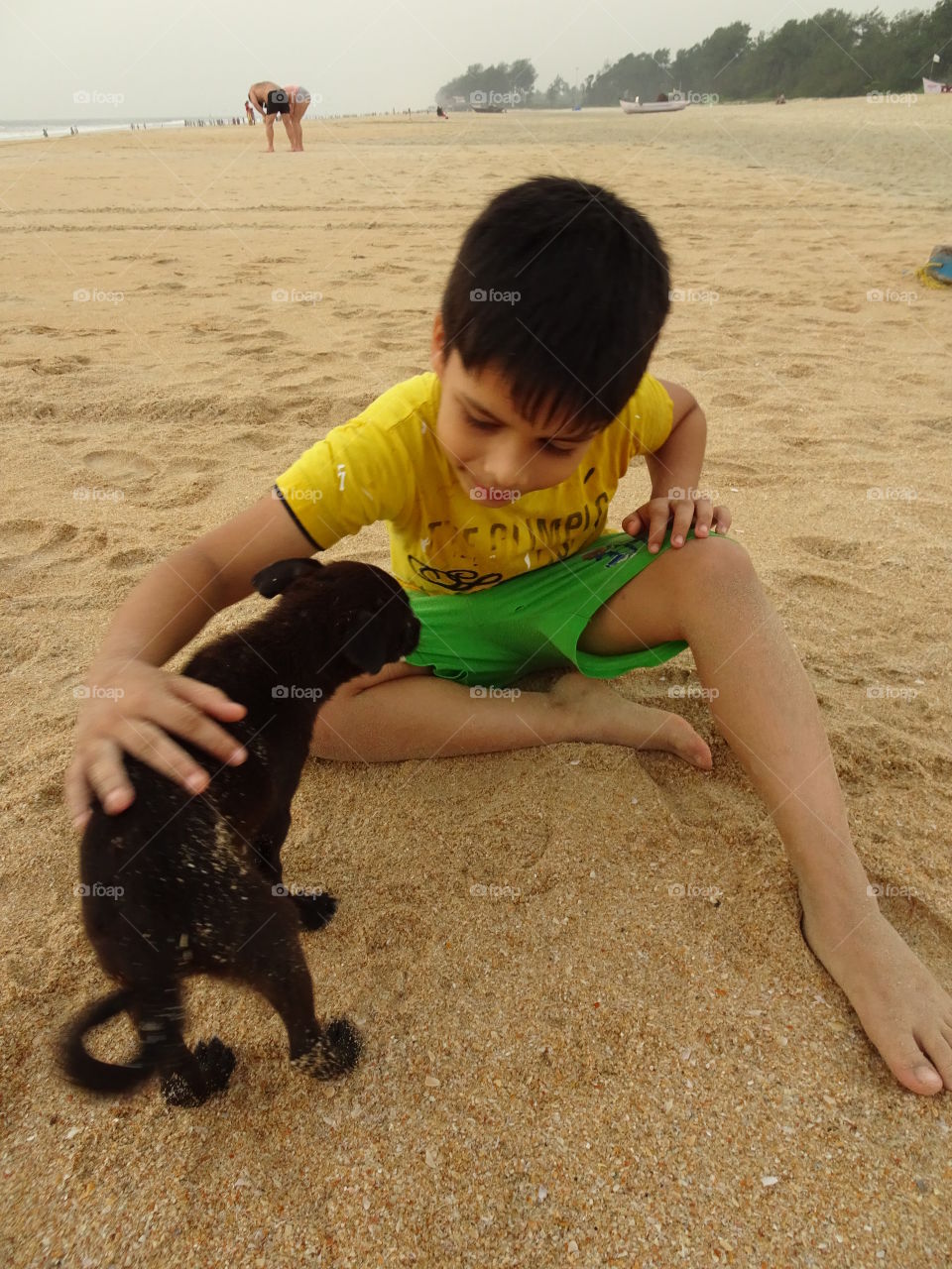 small kid playing with a street puppy on the beach
