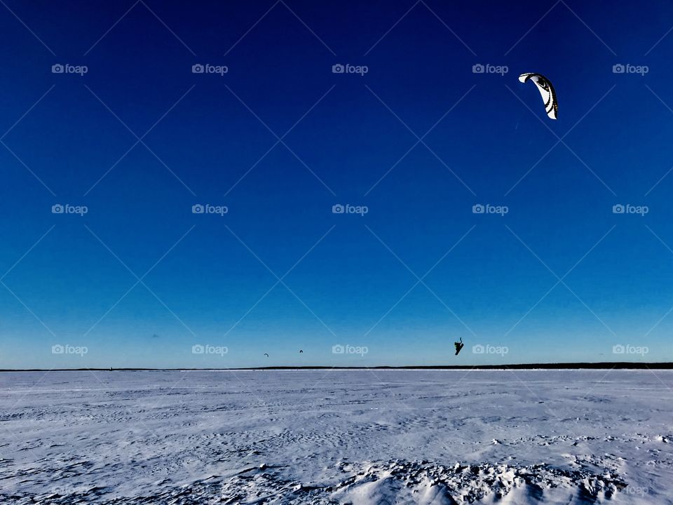 A parachute snowboarder on air on a frozen lake