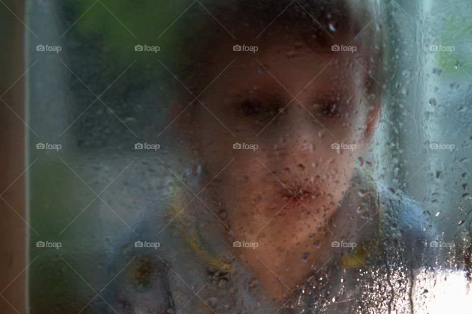 sad portrait of a boy through wed glass
