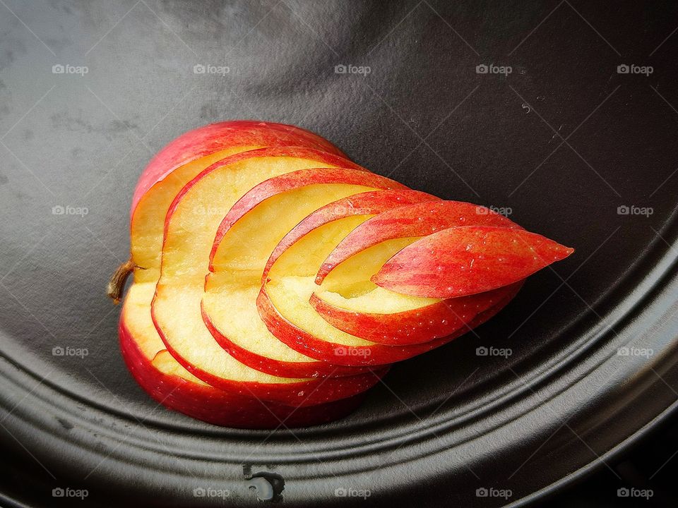 The red apple is cut in the shape of a leaf.  An apple in the form of a leaf lies on a black plate