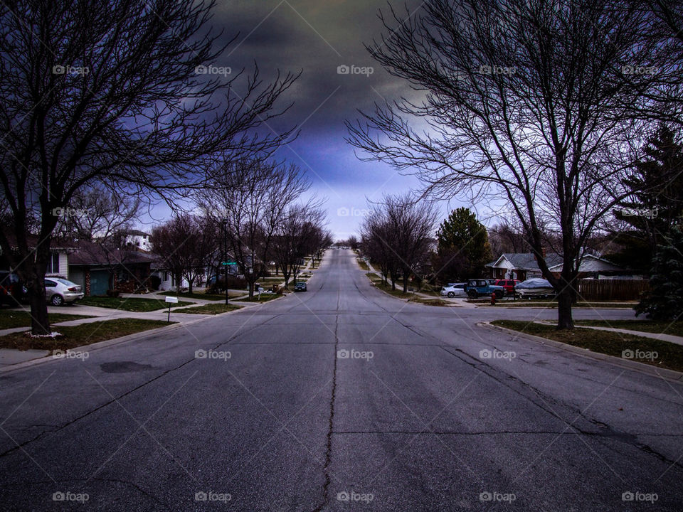 Straight forward road. Ominous clouds and peering trees.