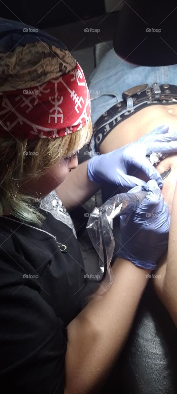 mujer rubia con cofia tatuando en cuerpo de un hombre se ven los detalles