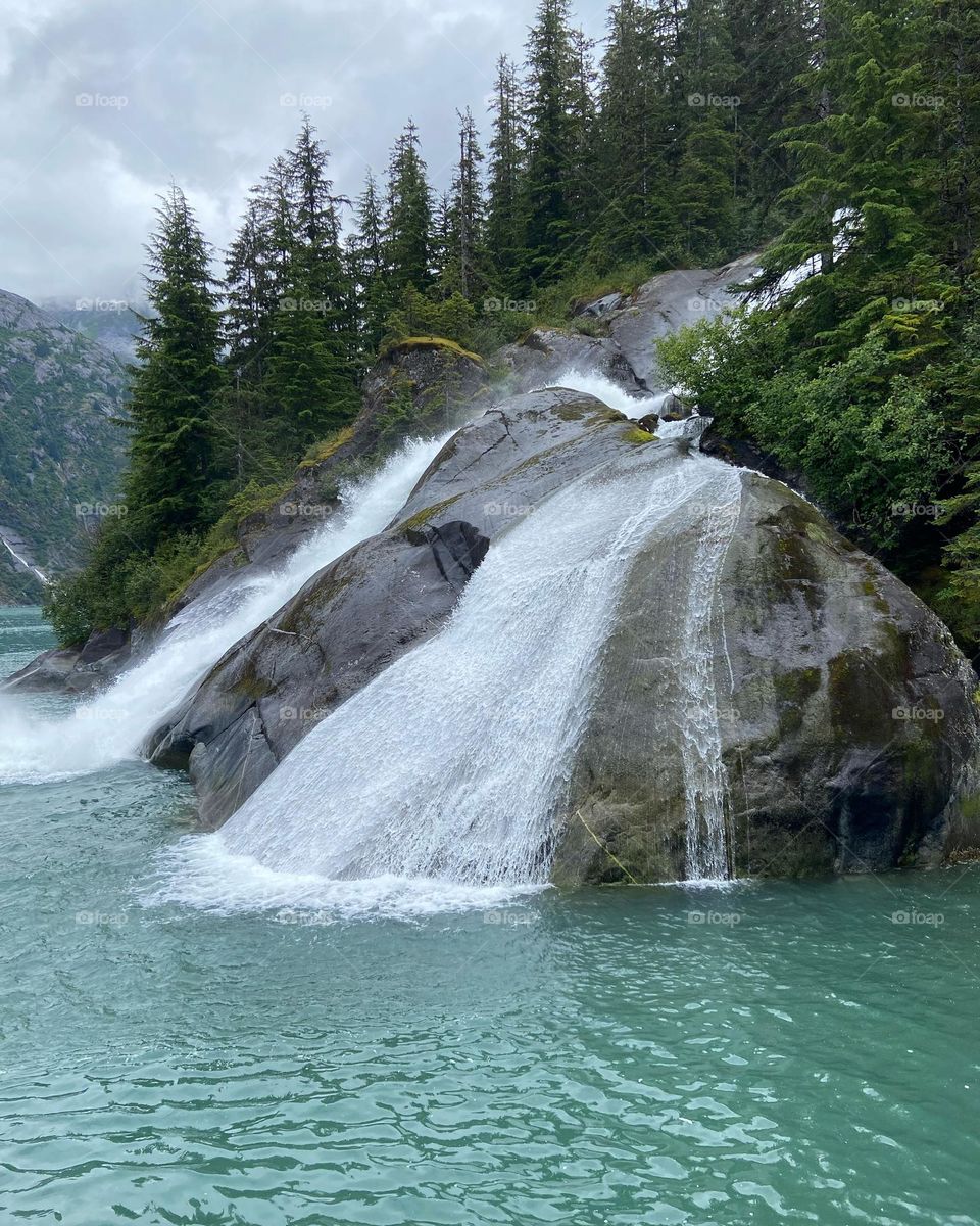 Nature at its finest. A waterfall cascading into the turquoise sea surrounded by tall green trees.