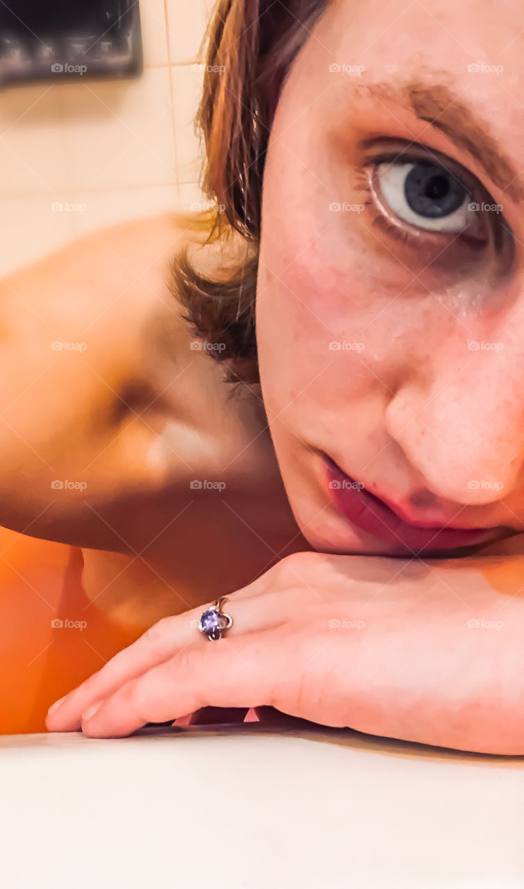 A teen girl poses in a bathtub full of pink water and wearing a violet ring from Bubbly Belle