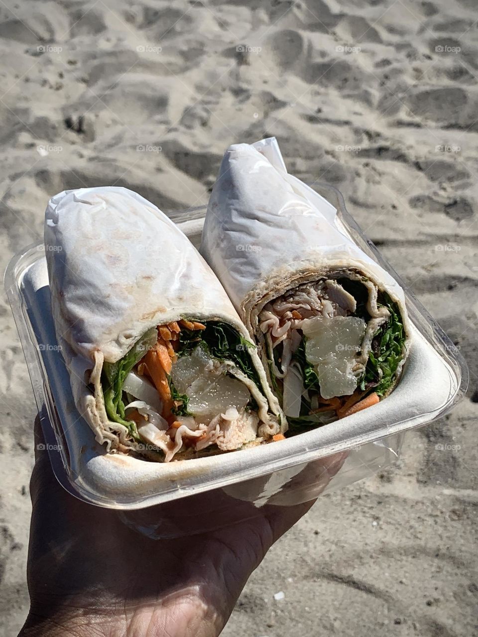 Turkey sandwich wrap on a person’s hand against sand background.