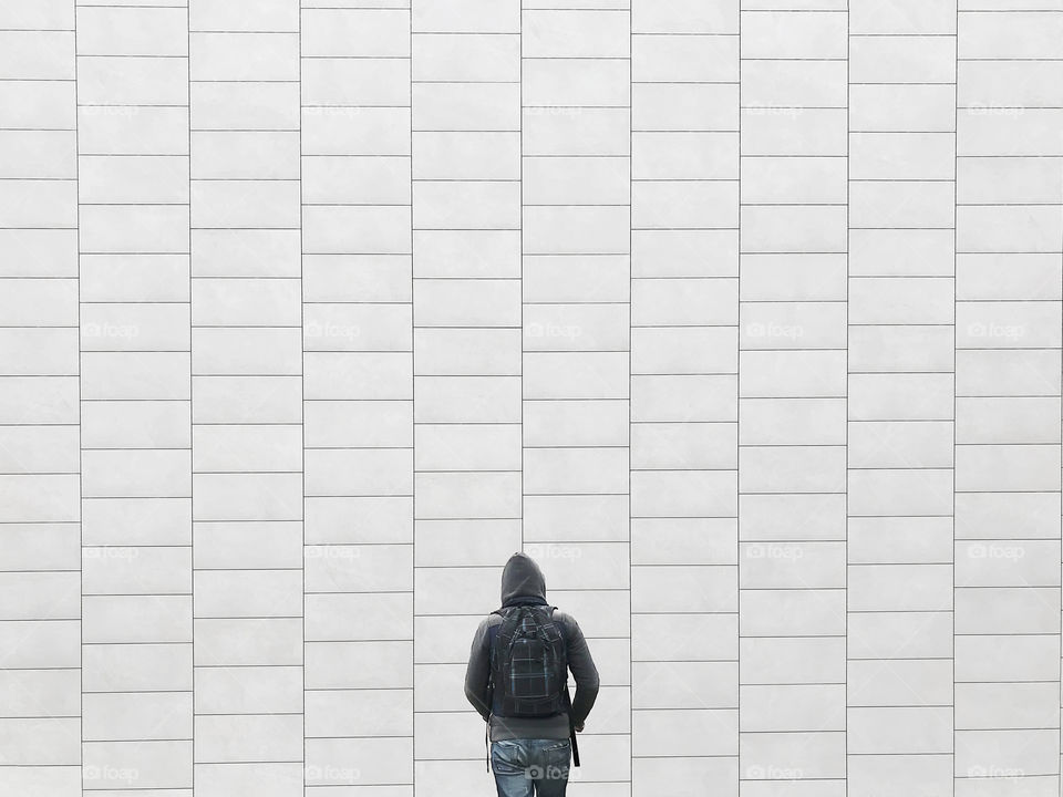 Young man with a backpack in front of a grey brick wall background 