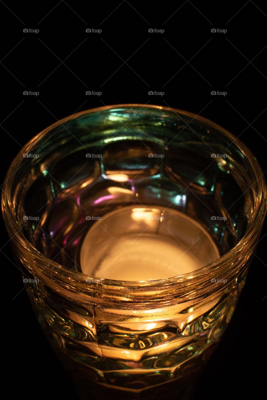 The flickering flame of a small candle through iridescent bubbled glass in the dark of night.