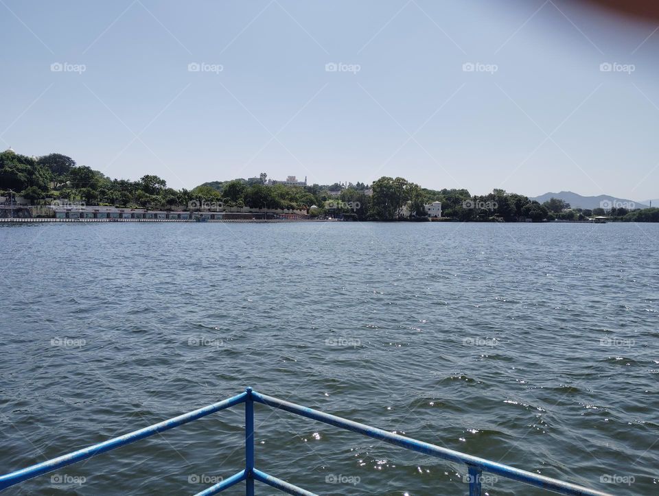 a landscape scene on a river with blue water, mountain, boat sky, green trees looks very beautiful