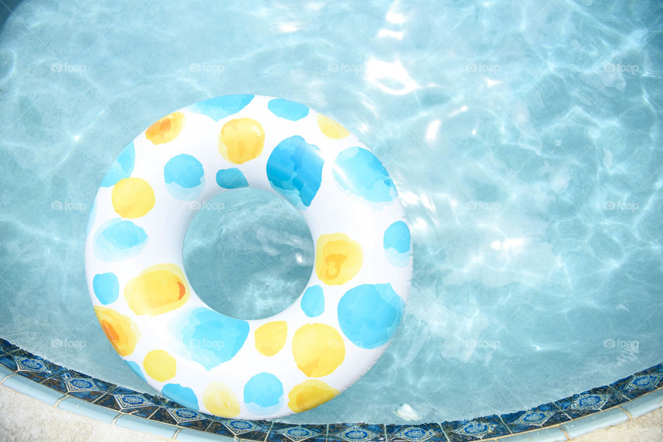 Overhead view of a blue spotted inner tube pool float on a crystal blue swimming pool surface