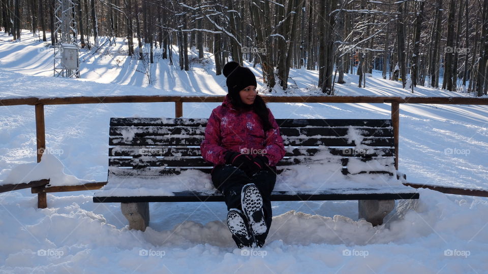 Hispanic girl sitting on a snowy beach at the mountain covered with snow 