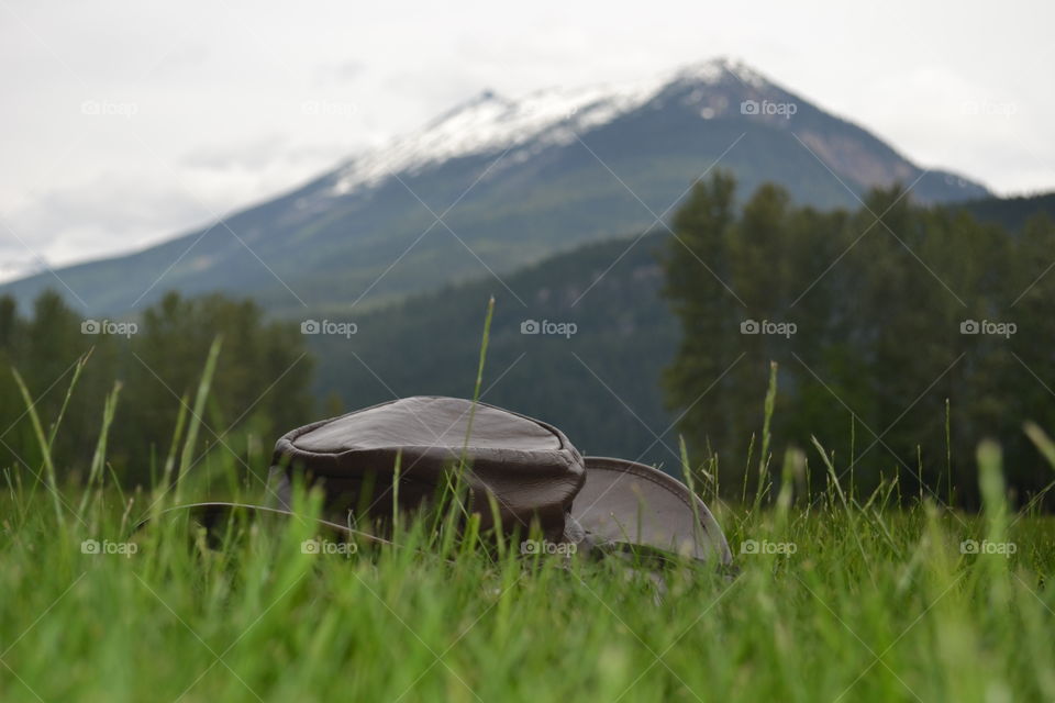Australian leather bush hat on grass in alpine meadow against backdrop of snow capped Rocky Mountains in Canada 