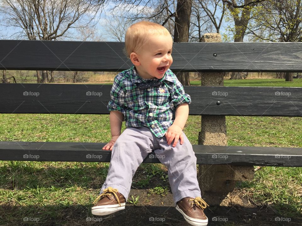 Cute baby boy sitting on bench at perk