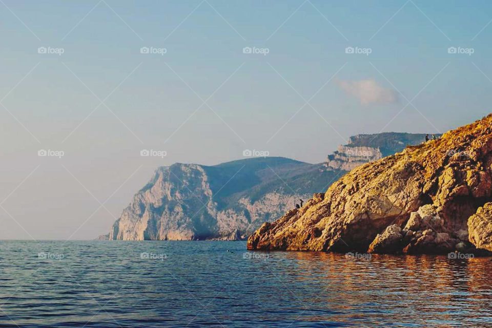 Long distance view of beautiful natural landscape with huge coral rocks in front and high hills or cliffs in the background, surrounded by calm sea water