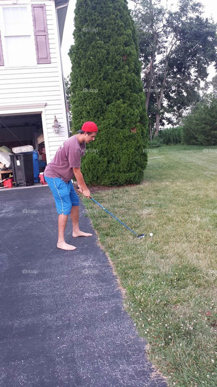 practicing his swing. teenage boy practices golf swing outside garage