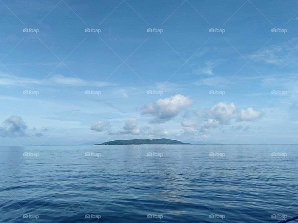 Island in the stream underneath the baby blue skies and clouds with relaxing calm sea.