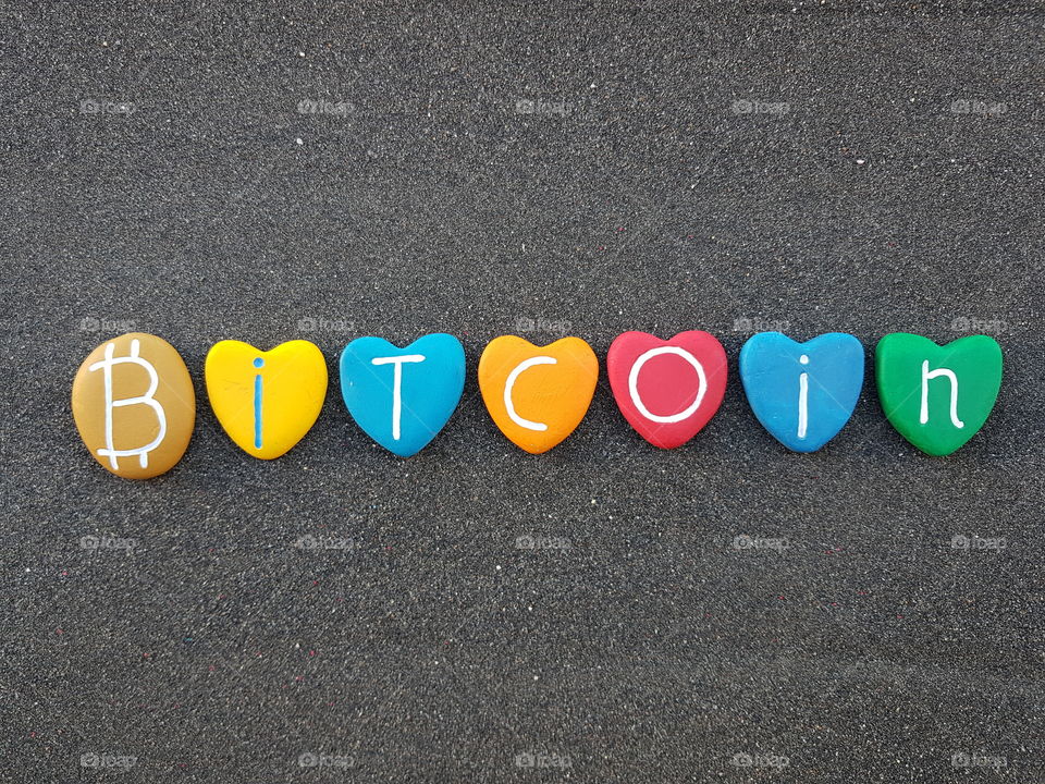 Bitcoin text with multicolored heart stones over black volcanic sand 