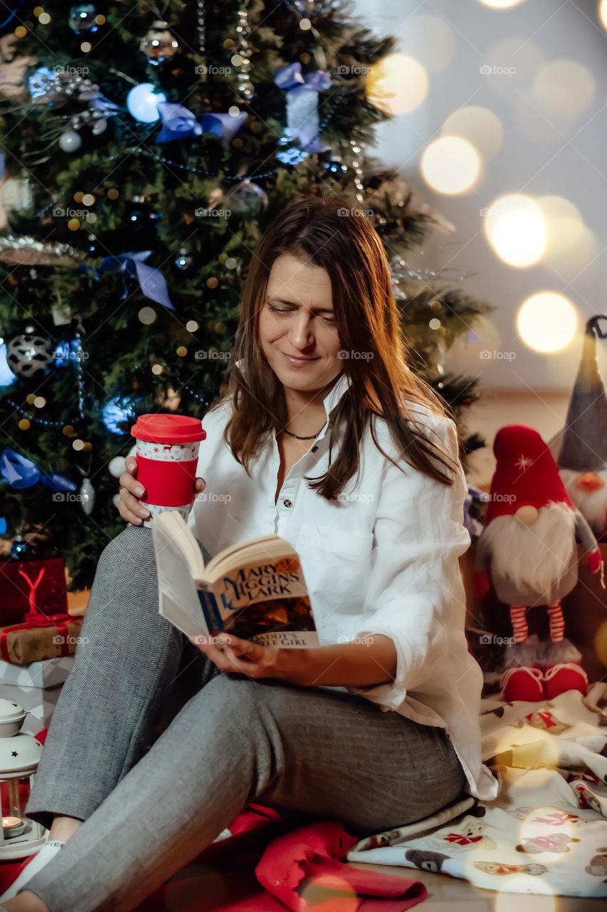 woman at home reading a book and drinking hot drink, christmas eve