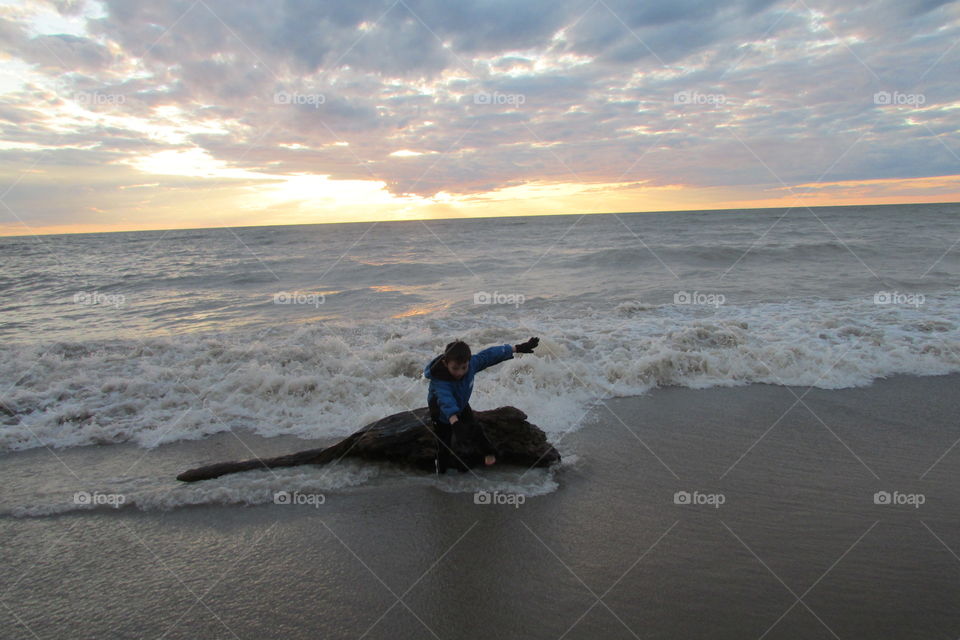 Boy jumping off driftwood as waves crash 