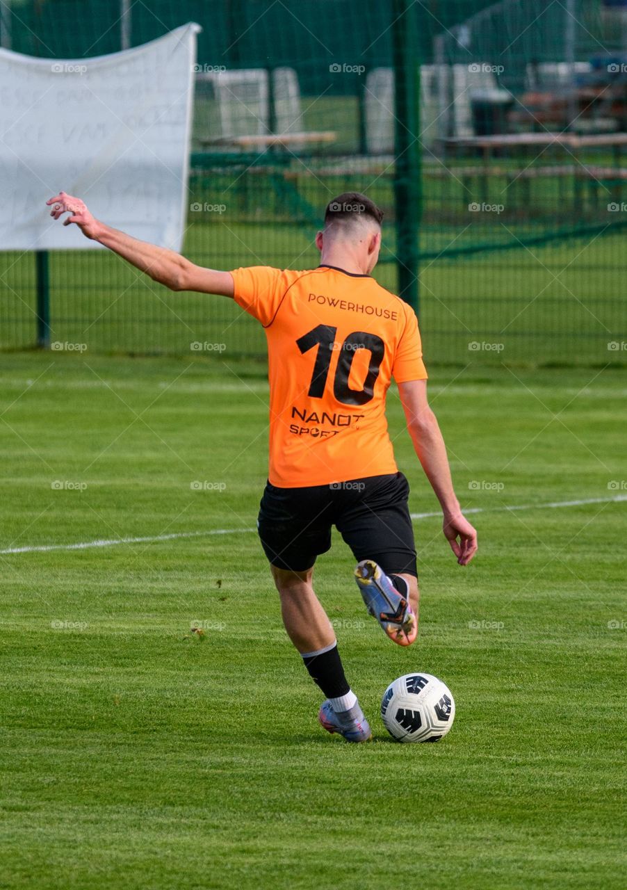 Rear view of young footballer wearing number 10 jersey, kicking a ball during an official match