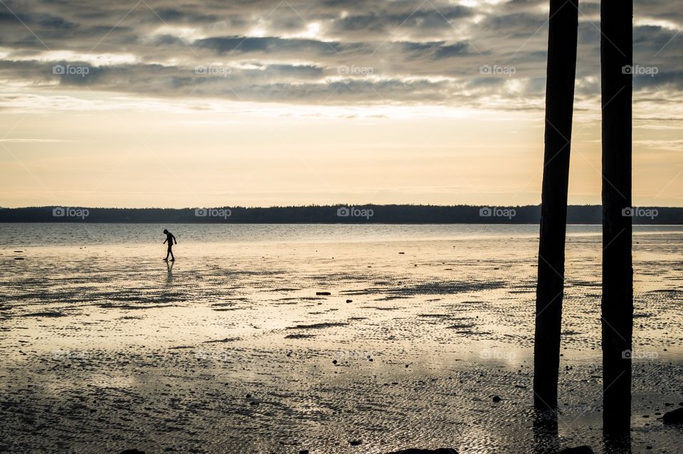 Walking on the beach. Tiny person walking alone on the beach at low tide just before sunset.