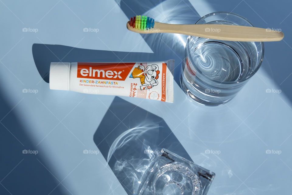 Elmex toothpaste for small children for oral and dental care, ecological toothbrush is on a blue background, with water, and a green flower.