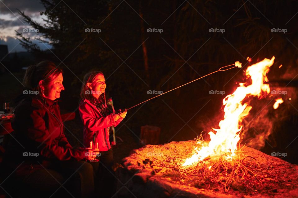 Family sitting at campfire during summer vacation. Mother and daughter spending time on summer weekend. Vacation trip close to nature