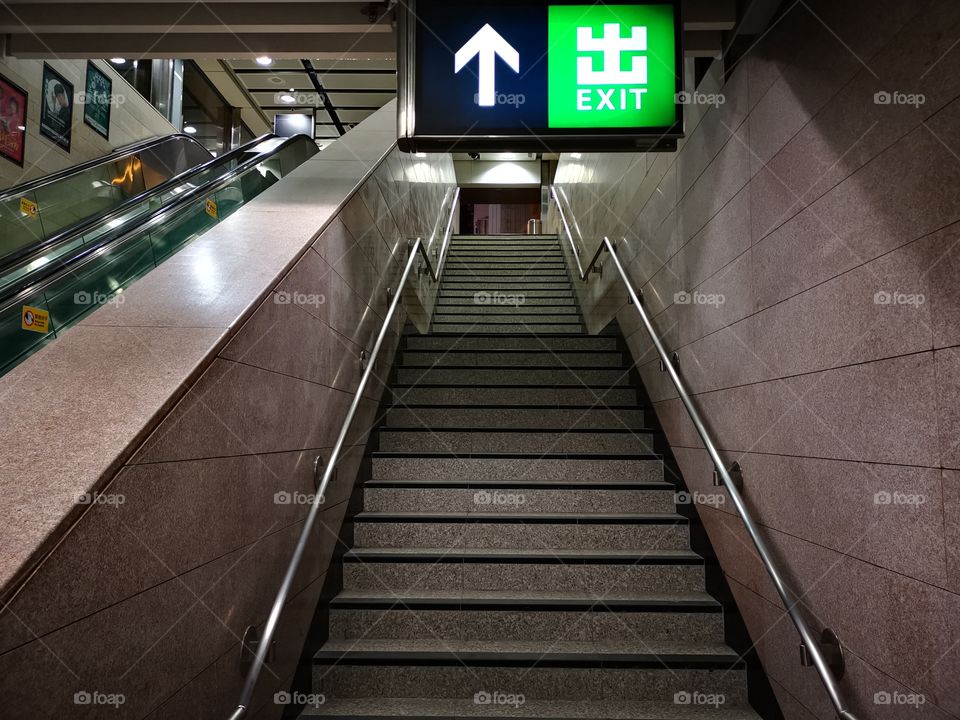 MTR exit sign with arrow looking up the stairs next to escalators in Hong Kong