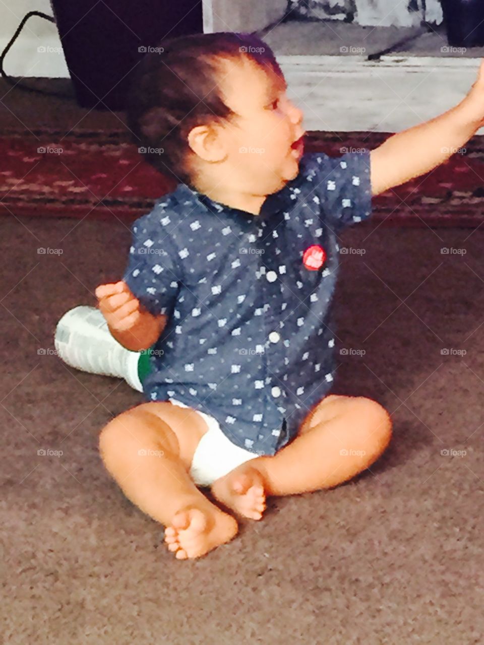 Little boy baby sitting on floor teaching out with his arm. 