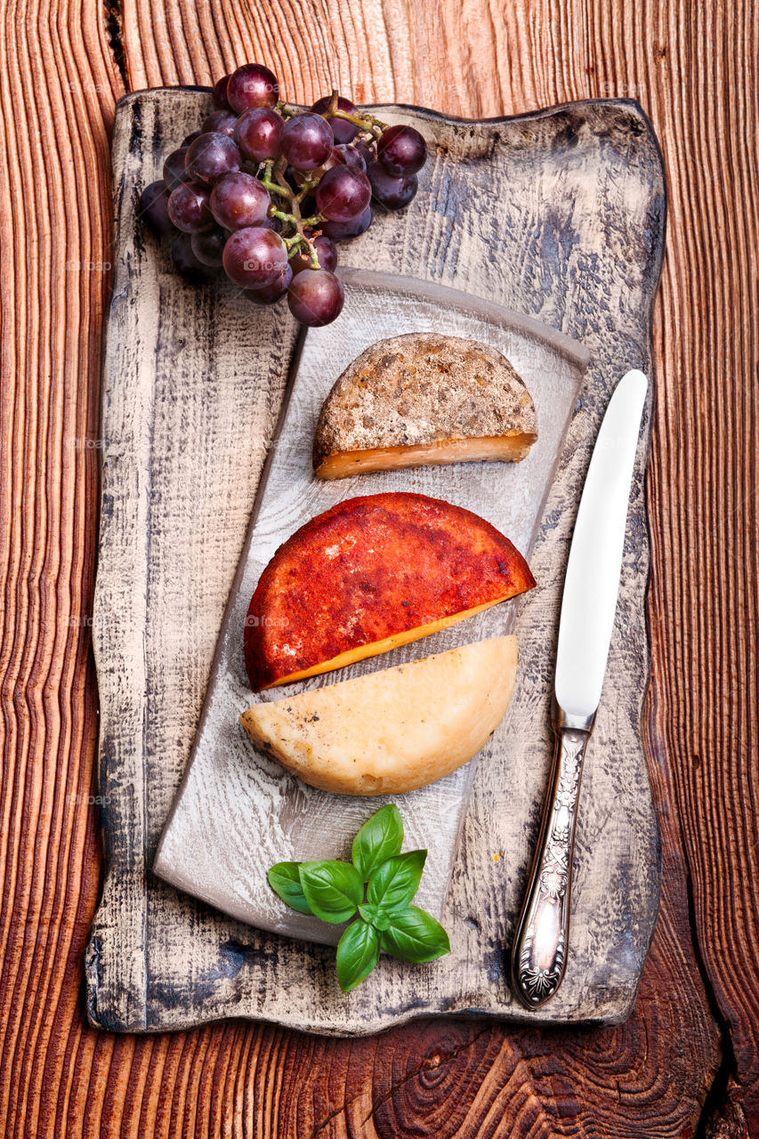 Cheese and black grapes decorated with mint on handmade pottery plate on old wooden table from above