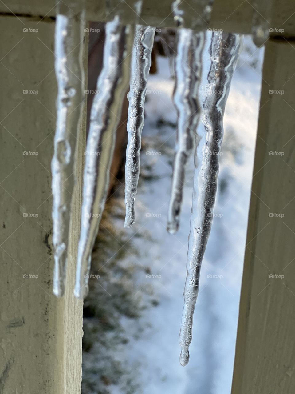 Clear icicles dripping from wooden porch banister on a warmer winter day in Maine.