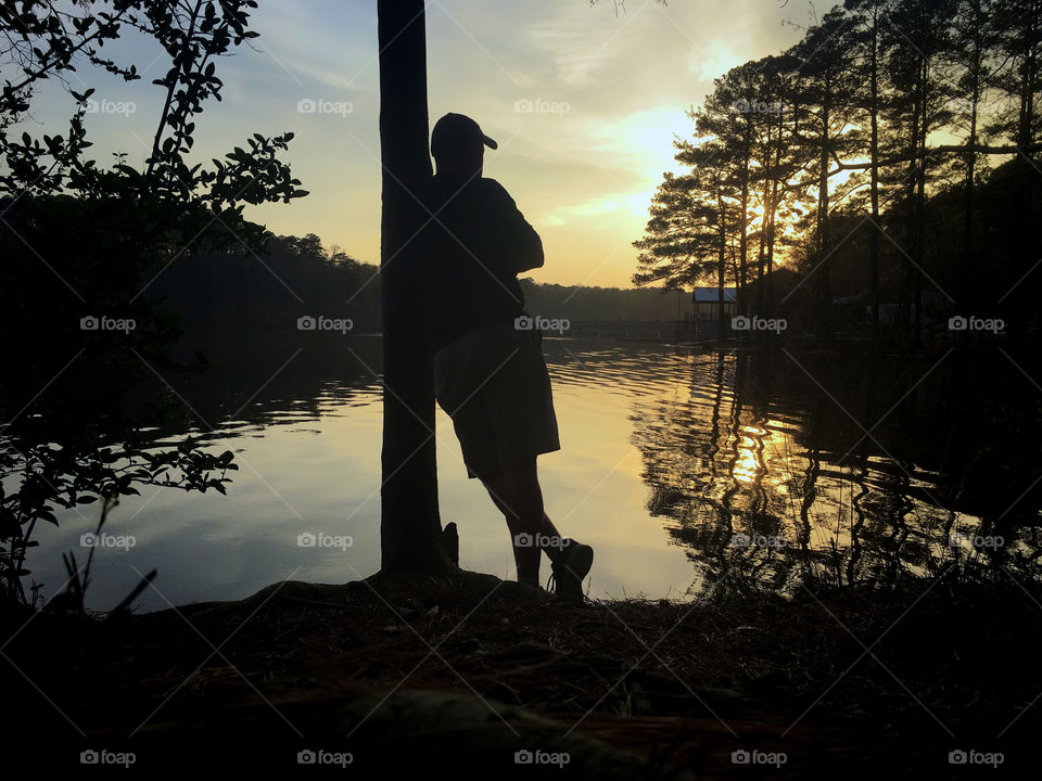 Man leaning on a tree at the lake during sunset pondering string theory and vibrations of energy...or what to get for supper. Lake Johnson Park in Raleigh North Carolina, Triangle area, Wake County. 