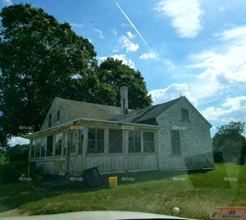 Farm house on land near vegetable stand. Trees, grass, older home.