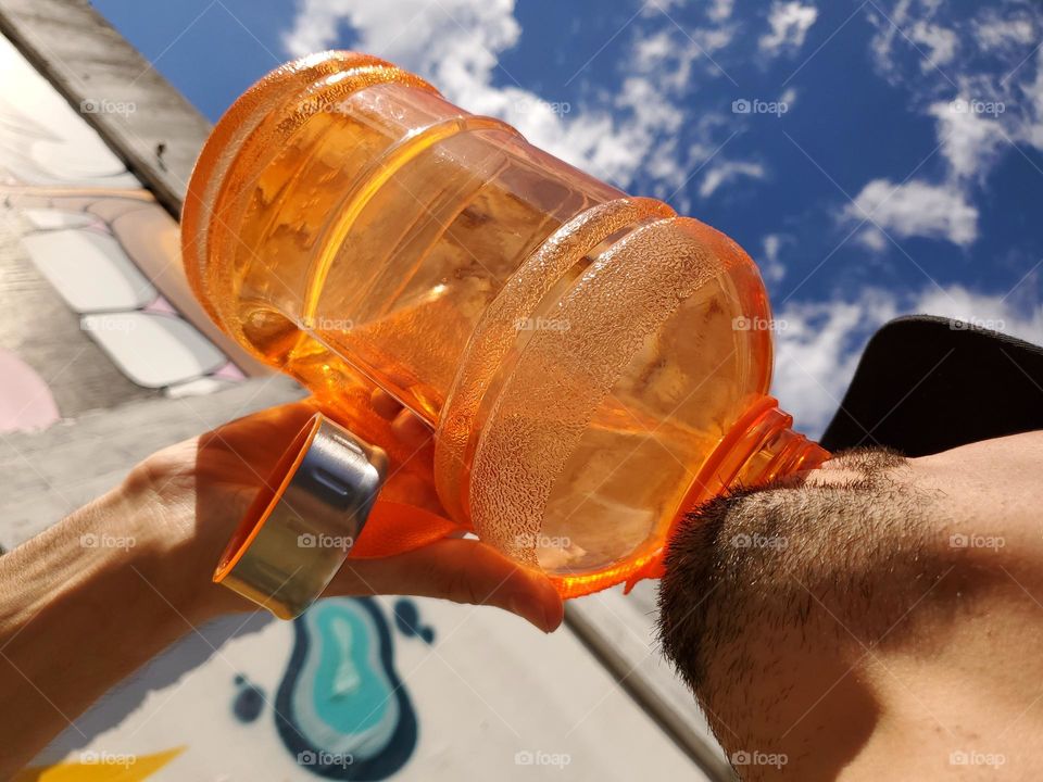 Liquids are cool- Man drinking water from an orange water bottle.