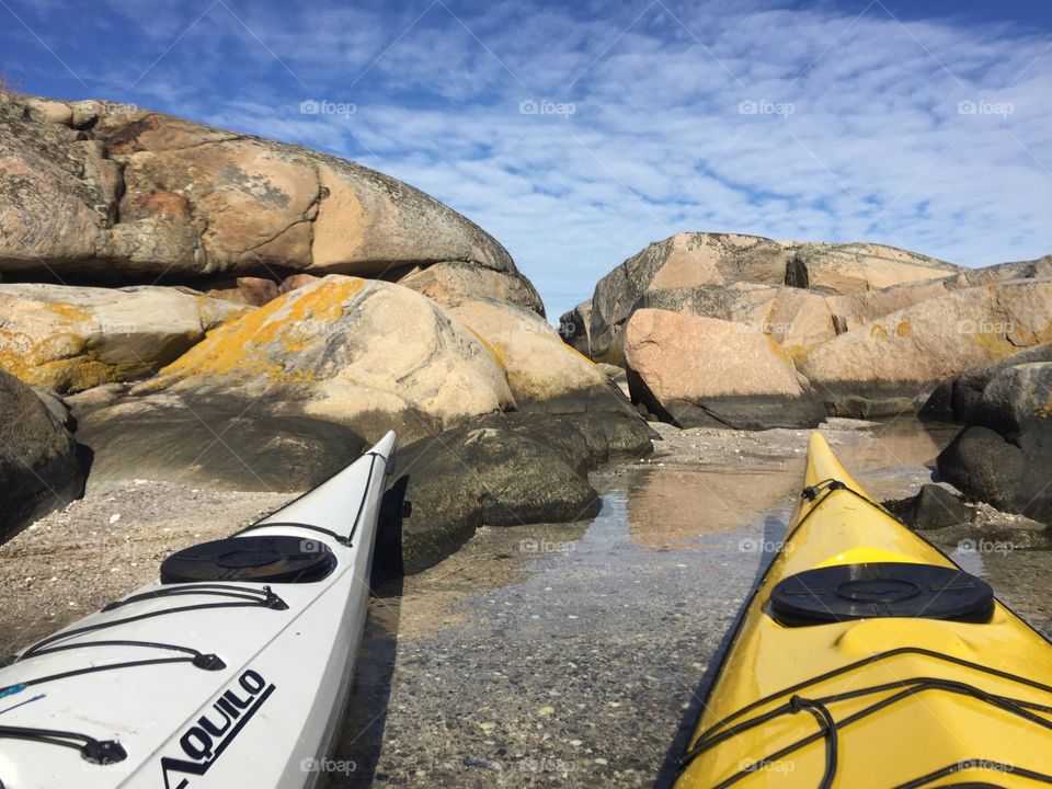 Rocks and two kayaks . Kayaks on the beach. Blue sky with white clouds.