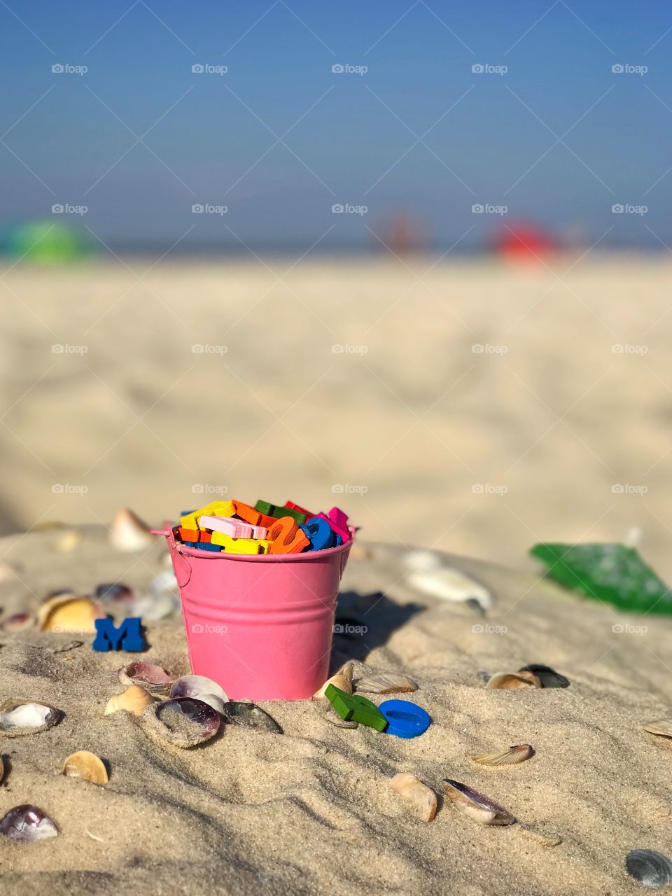 pink baby iron bucket filled with wooden colorful letters stands on the sand on the background of the sea