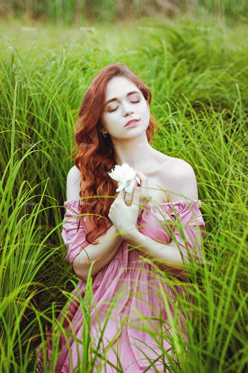 Portrait of beautiful young redhead woman, girl in pink dress sitting  outdoor, in the summer park, meadow with green grass